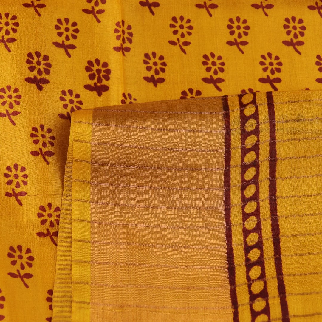 Close-up of the yellow printed Tussar silk saree's distinct slubby fabric texture.