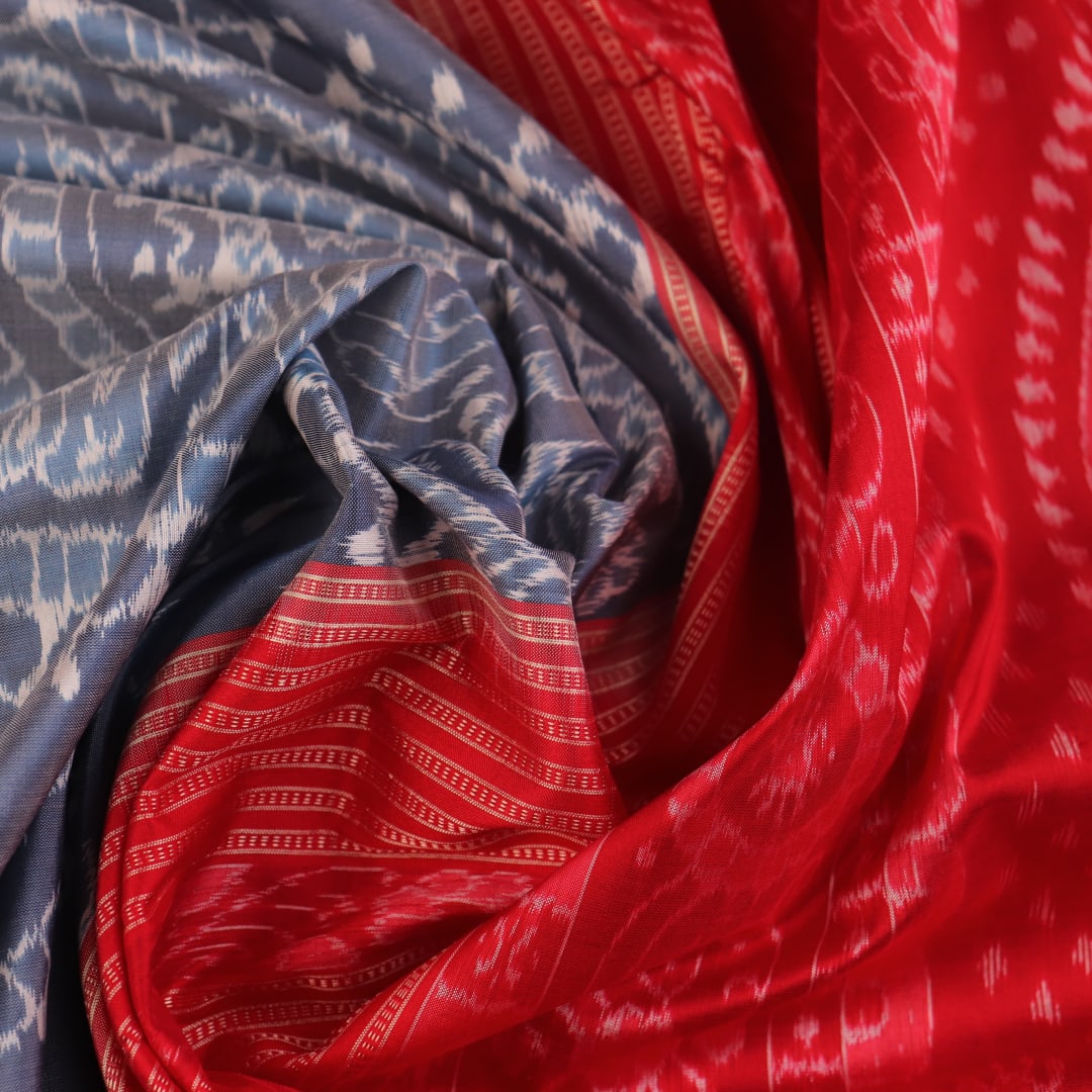 Close-up of grey and red Sambalpuri silk saree fabric showing intricate woven motif texture.