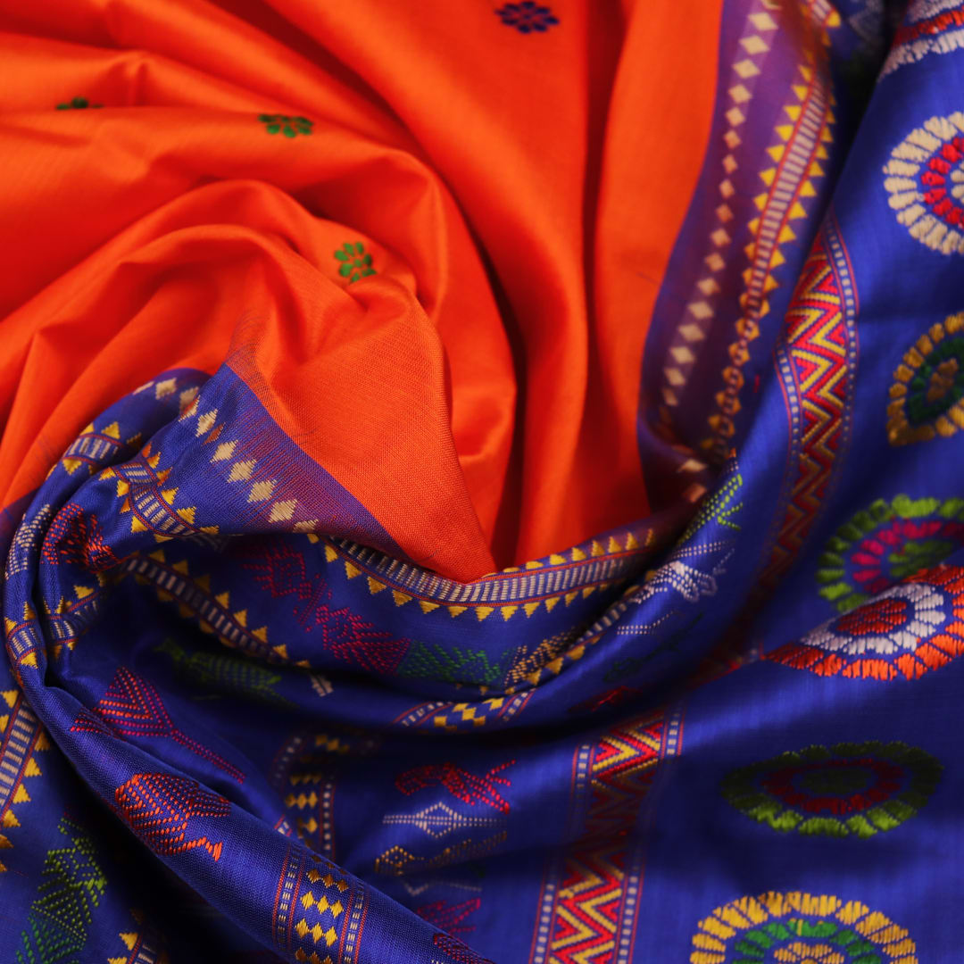 Close-up view of the vibrant orange and blue silk fabric texture with intricate butta pattern