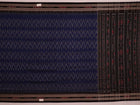 A person wearing a vibrant blue cotton Sambalpuri saree with black motifs, styled in a traditional drape.