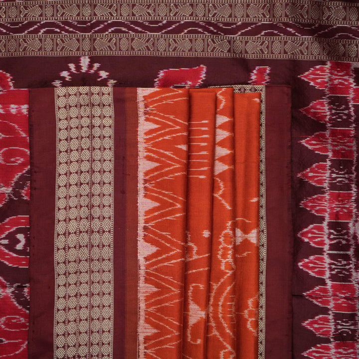 Extreme close-up of the lustrous rust Sambalpuri silk fabric, showing its fine weave and subtle motif texture.