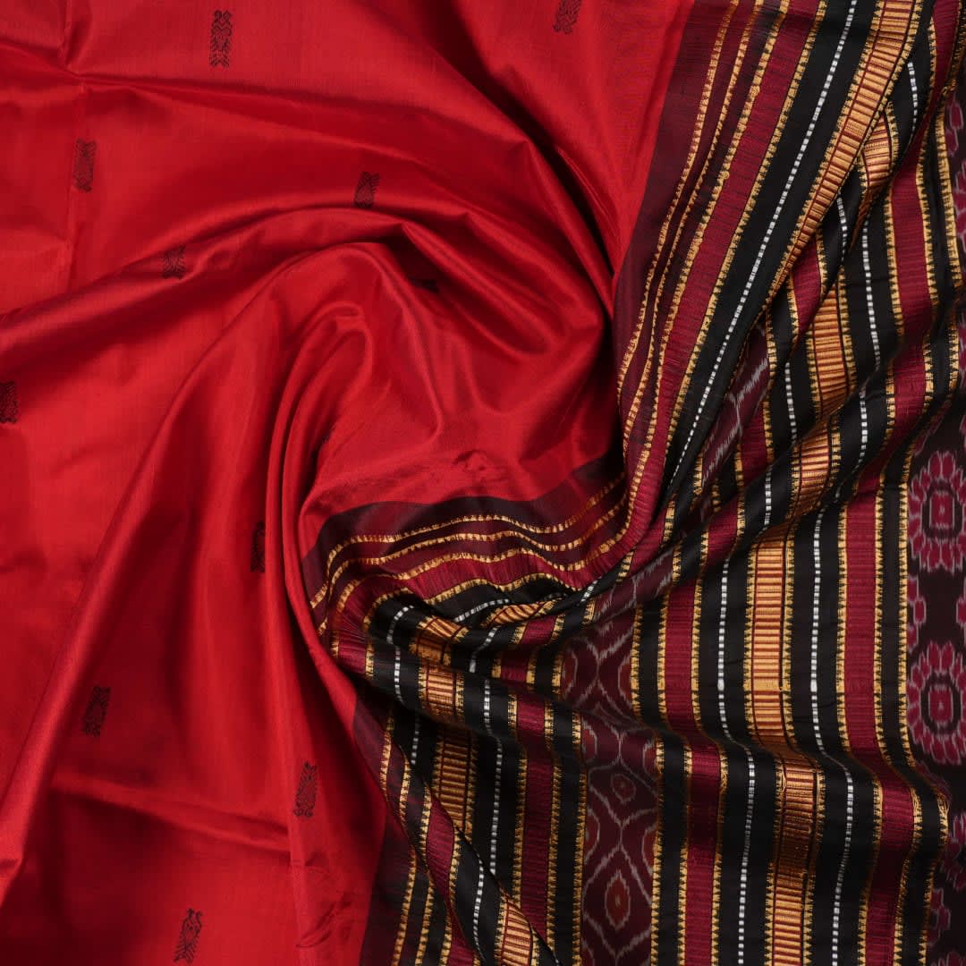 Detailed view of hand-woven silk fabric texture and butta patterns on a red Sambalpuri saree.
