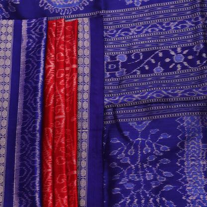 Close-up of red Sambalpuri silk saree fabric showing intricate woven motif texture and subtle blue threads.