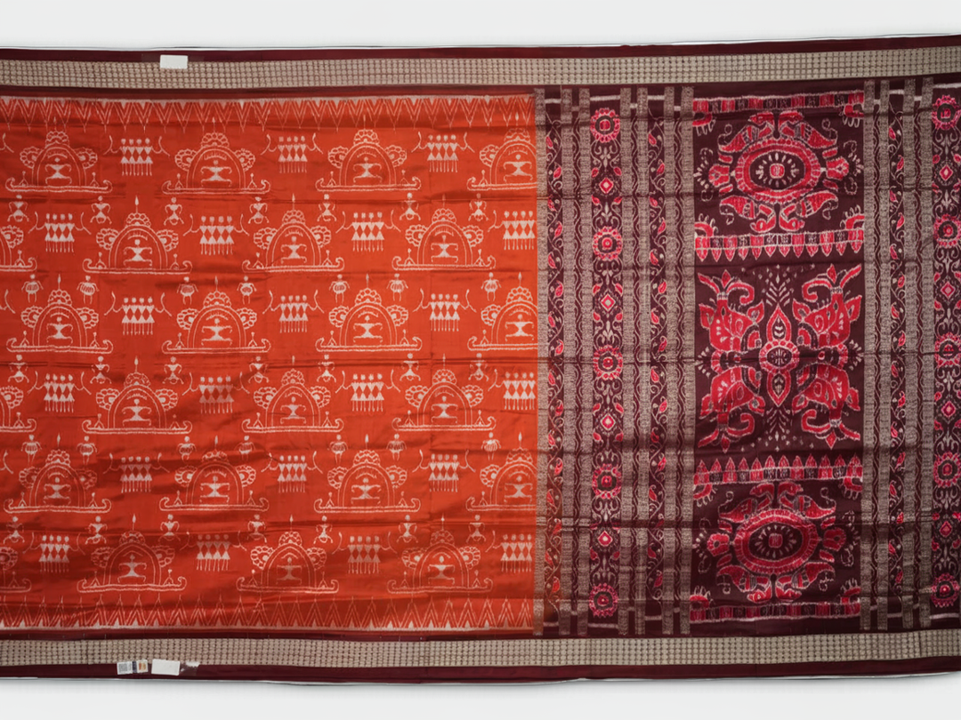 Extreme close-up of the lustrous rust Sambalpuri silk fabric, showing its fine weave and subtle motif texture.