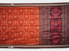Extreme close-up of the lustrous rust Sambalpuri silk fabric, showing its fine weave and subtle motif texture.