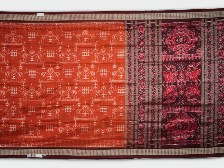 Extreme close-up of the lustrous rust Sambalpuri silk fabric, showing its fine weave and subtle motif texture.