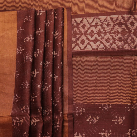 Close-up of the brown Tussar silk saree fabric, highlighting its natural slub texture and printed pattern.