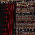 Close-up texture of handwoven Bomkai silk saree fabric: maroon and black threads forming butta pattern.