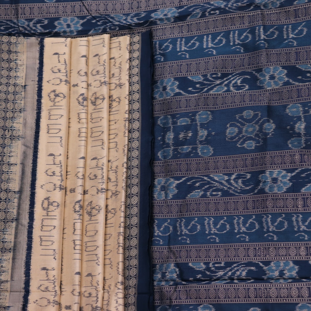 Close-up detail of the cream-colored silk fabric texture with blue motifs in Sambalpuri saree