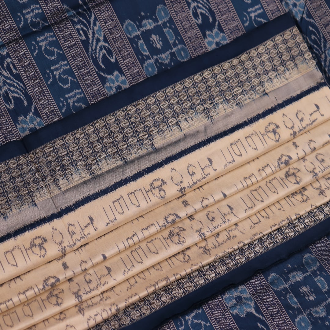 Close-up detail of the cream-colored silk fabric texture with blue motifs in Sambalpuri saree