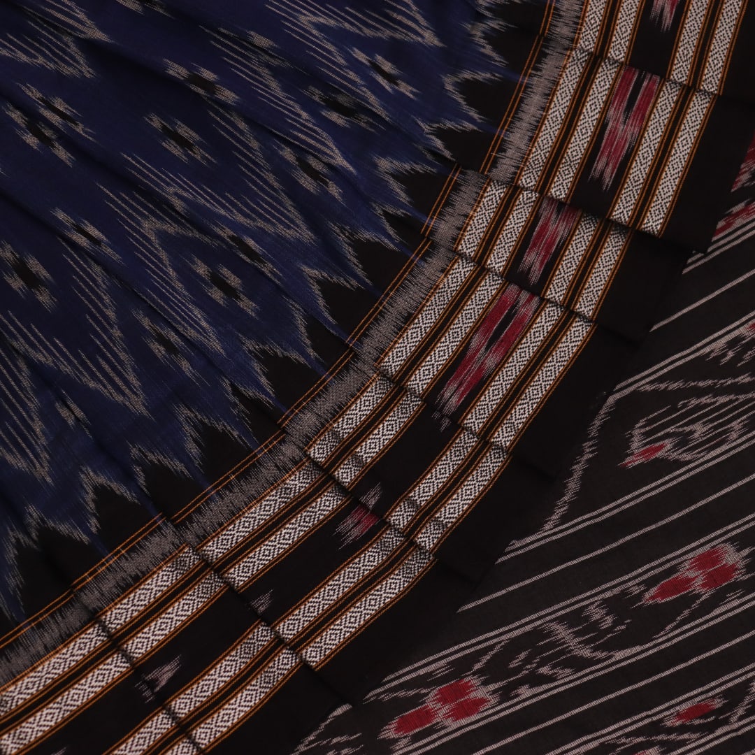 A person wearing a vibrant blue cotton Sambalpuri saree with black motifs, styled in a traditional drape.