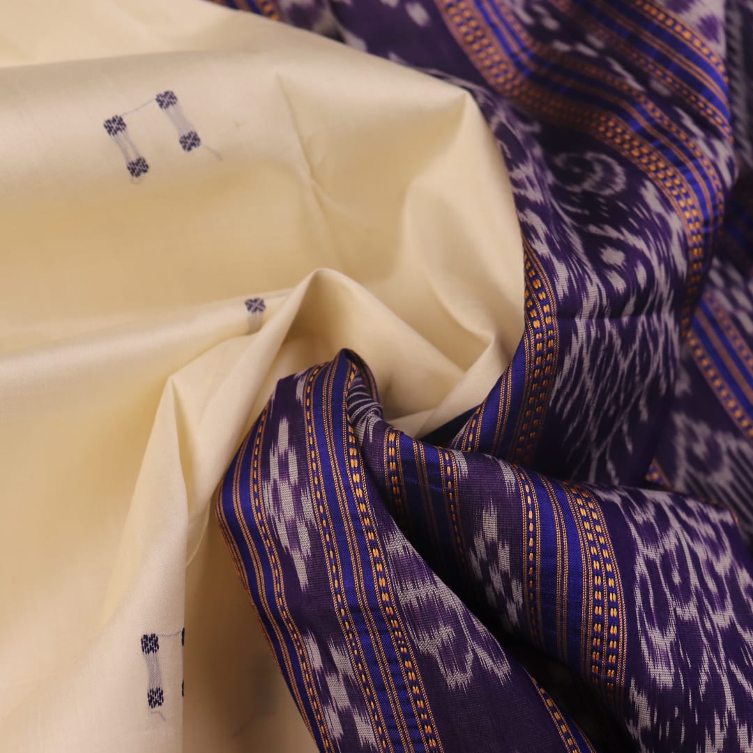 Woman elegantly draped in a white and blue Khandua silk saree with butta pattern.