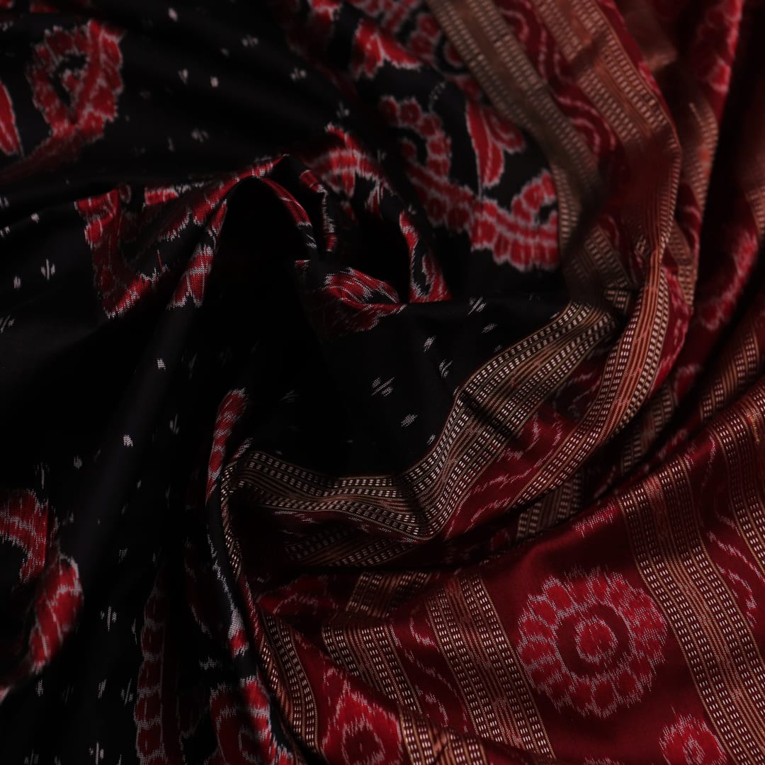 An approximately 150 cm wide handloom black silk Sambalpuri Saree with maroon motifs, captured in a close-up to depict its rich fabric texture.