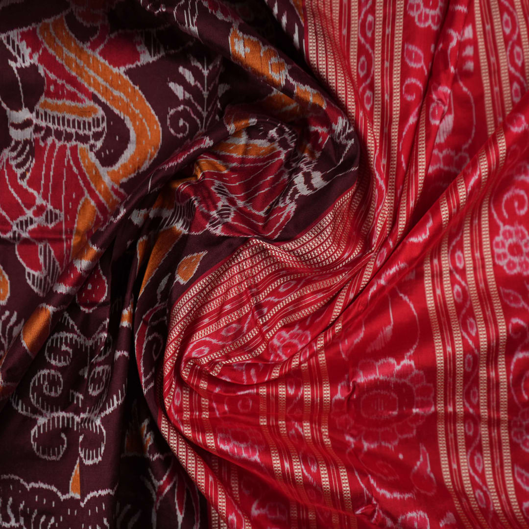 Close-up of the maroon Sambalpuri silk saree fabric, highlighting its luxurious texture and intricate weave.