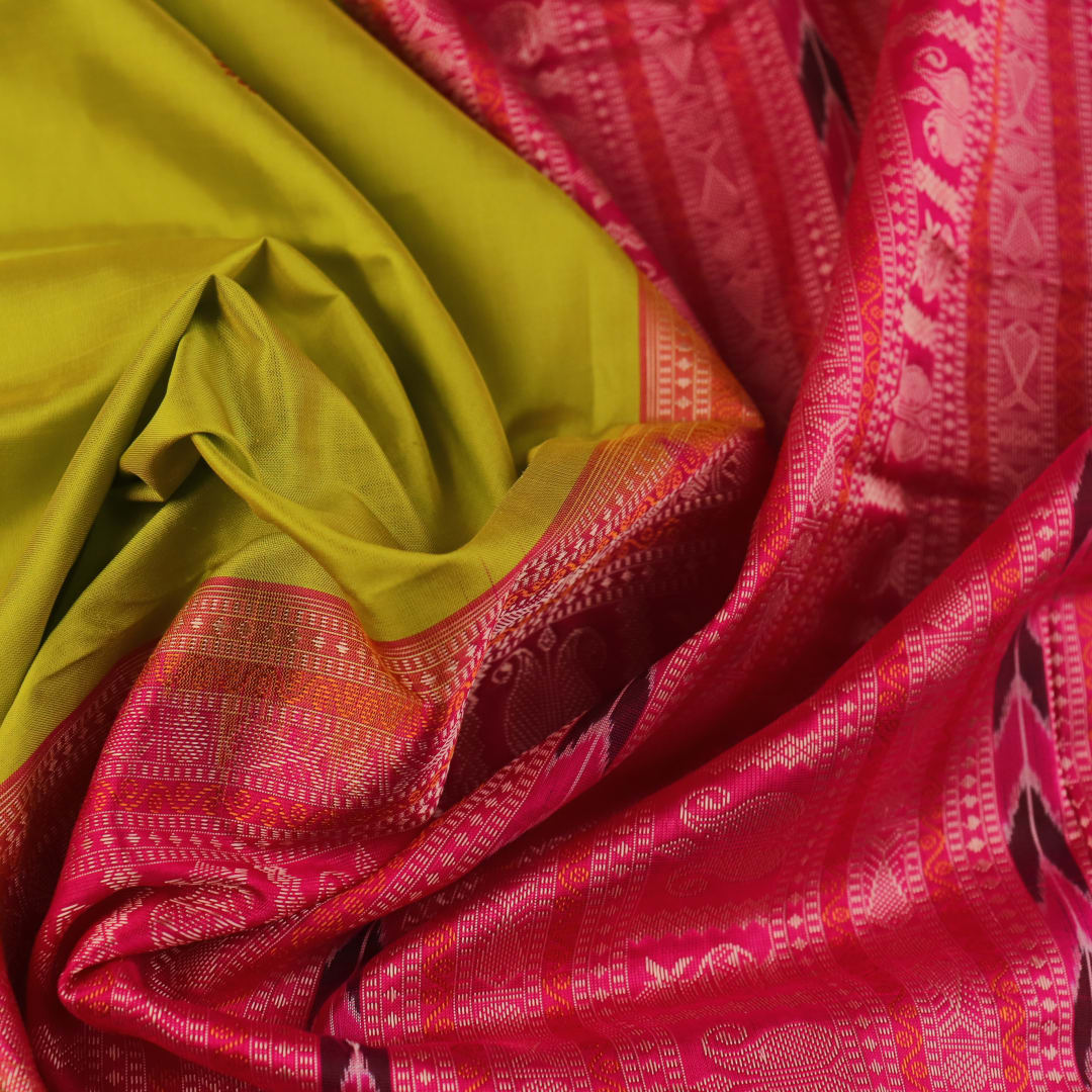 Close-up of green and magenta Bomkai silk saree fabric texture, highlighting intricate weave and butta pattern.