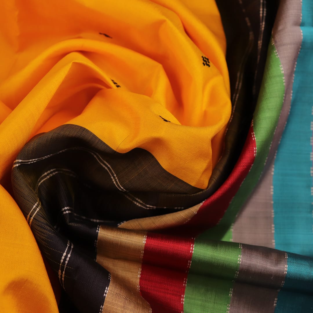 Close-up view of the golden silk fabric with black butta pattern of a Berhampuri silk saree