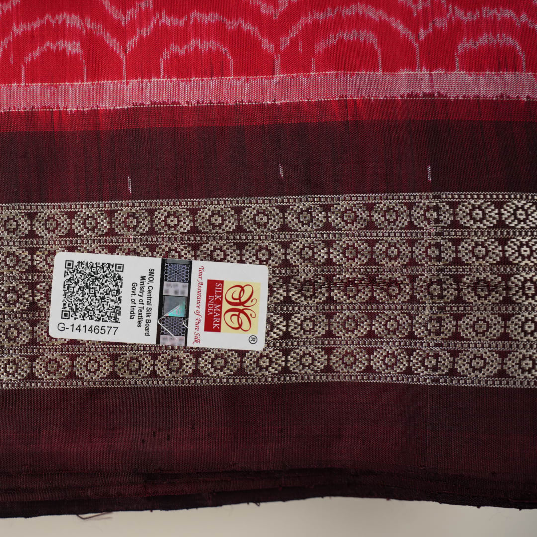 Ultra close-up of the red Sambalpuri silk saree fabric, revealing its luxurious texture and handloom weave.