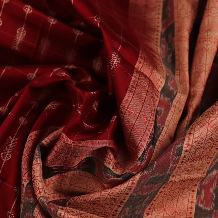 Close-up view of the richly textured silk fabric of a maroon and off-white Sambalpuri saree, featuring a delicate butta pattern.