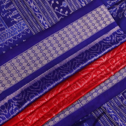 Close-up of red Sambalpuri silk saree fabric showing intricate woven motif texture and subtle blue threads.