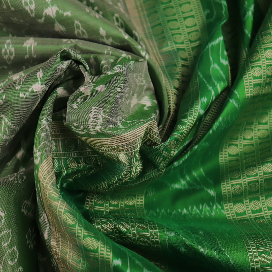 Close-up view of the intricate silk fabric texture of a green Sambalpuri silk saree with traditional motifs.