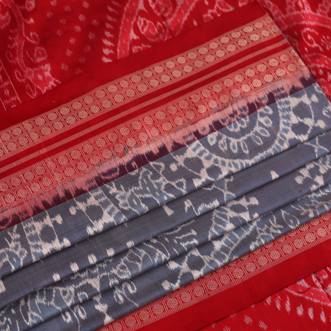 Close-up of grey and red Sambalpuri silk saree fabric showing intricate woven motif texture.